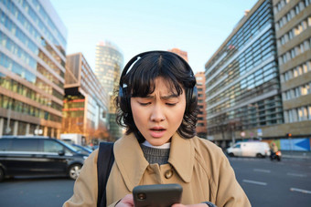 肖像年轻的亚洲女孩学生走城市听音乐耳机移动电话街道有关屏幕阅读坏新闻