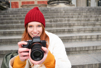 年轻的学生摄影师坐在街楼梯检查照片专业相机采取照片在户外
