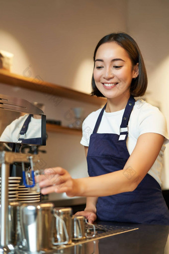 肖像可爱的咖啡师<strong>女孩</strong>工作计数器使咖啡热气腾腾的牛奶卡布奇诺咖啡穿咖啡馆统一的蓝色的<strong>围裙</strong>
