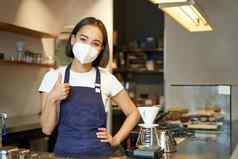 科维德流感大流行概念友好的咖啡师女孩医疗面具作品咖啡馆计数器啤酒咖啡客户显示拇指
