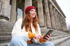 肖像年轻的城市女孩红色的他坐在楼梯博物馆持有移动电话连接公共无线网络冲浪网智能手机应用程序