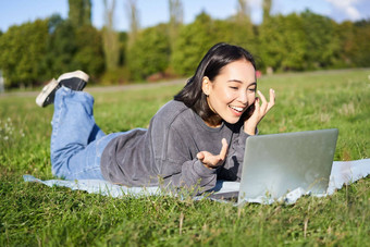 快乐亚洲女孩会说话的朋友移动PC<strong>视频</strong>聊天说谎公园毯子阳<strong>光</strong>明媚的温<strong>暖</strong>的一天