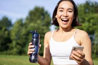 兴奋年轻的亚洲女人<strong>锻炼</strong>饮料水体育应用程序智能手机惊讶快乐<strong>锻炼公园</strong>
