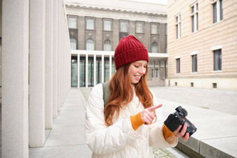 微笑红色头发的人女孩摄影师采取图片城市使照片在户外专业相机