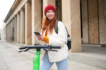 美丽的年轻的女人旅游背包租金e-scooter旅行小镇移动电话应用程序