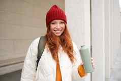 年轻的快乐红色头发的人女人红色的他喝热水瓶气候变暖热喝瓶走城市旅游放松温暖的刷新