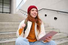 快乐红色头发的人女人红色的他坐在楼梯在户外平板电脑连接无线网络公共建筑读取数字书等待街