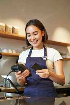 肖像微笑亚洲咖啡师咖啡商店员工回来终端信贷卡帮助客户端支付非接触式咖啡馆