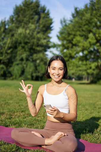 垂直拍摄亚洲女人显示<strong>标志推荐</strong>瑜伽培训在线冥想应用程序练习新鲜的空气公园