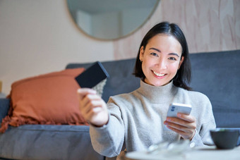 微笑可爱的亚洲女人信贷卡智能手机支付账单在线持有移动电话相机