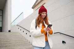 红色头发的人女孩年轻的女人旅游背包持有智能手机路线移动应用程序搜索酒店电话地图微笑幸福的