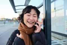 关闭亚洲女孩公共汽车停止笑着说电话谈话会谈电话等待公共运输穿冬天衣服