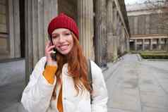 微笑红色头发的人女旅游会谈移动电话走城市快乐学生红色的他调用朋友站街智能手机