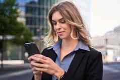 关闭肖像年轻的企业女人黑色的西装持有智能手机发短信消息站街移动应用程序