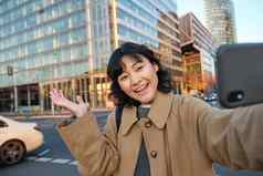 微笑朝鲜文女孩显示城市采取自拍前面建筑街快乐脸需要照片智能手机相机