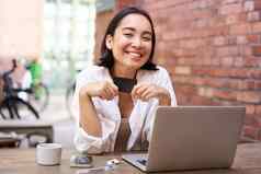 快乐年轻的亚洲女坐着移动PC显示信贷卡支付账单在线购物互联网坐着咖啡馆咖啡