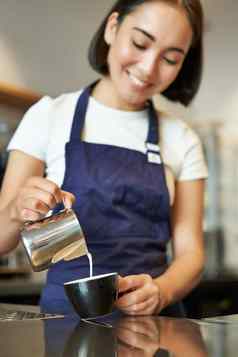 垂直拍摄浅黑肤色的女人亚洲女孩咖啡师穿围裙使咖啡准备订单咖啡馆倒牛奶杯卡布奇诺咖啡拿铁艺术