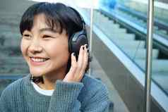肖像微笑朝鲜文女孩耳机智能手机坐在楼梯购物中心手表视频移动电话