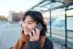 关闭年轻的亚洲女人会谈移动电话谈话电话等待公共汽车公共运输停止