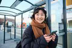 美丽的年轻的女人站公共汽车停止等待公共运输移动电话智能手机应用程序