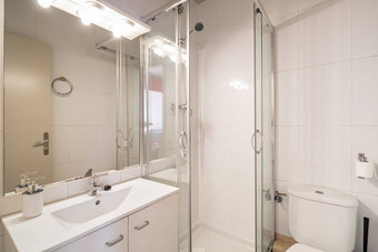 浴室光米色墙角落里淋浴玻璃滑动门虚荣水槽白色家具镜子照亮明亮的灯反射前面通过