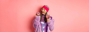 花俏的高级女人有趣的吃甜甜圈喝粉红色的香槟站<strong>紫色</strong>的人造皮毛<strong>外套</strong>闪闪发光的衣服工作室背景