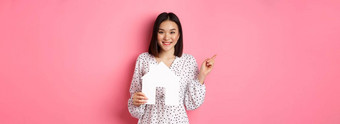 真正的房地产兴奋亚洲女人显示纸房子模型指出左复制空间站粉红色的背景