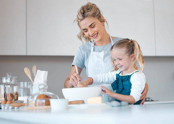 快乐妈妈。帮助女儿烤父烘焙孩子年轻的女人帮助女儿使面糊女孩混合碗面糊微笑家庭烘焙厨房