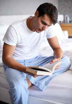 抓住了好书英俊的年轻的男人。阅读书边缘床上