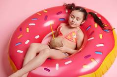 可爱的孩子女孩放松充气donought游泳环椰子鸡尾酒手孤立的粉红色的背景