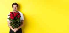 有趣的年轻的推销员黑色的围裙持有花束玫瑰花店笑站黄色的背景