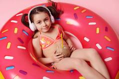前视图可爱的婴儿女孩耳机泳衣椰子树喝色彩斑斓的充气游泳环粉红色的背景