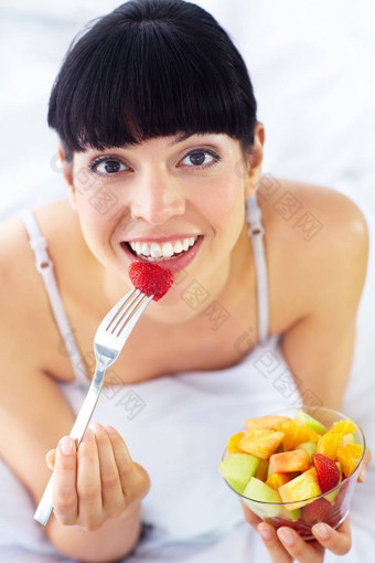 垮掉的一代健康的零食可爱的年轻的女人享受水果沙拉说谎床上