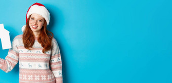 假期广告片真正的房地产概念快乐的红色头发的人女人圣诞老人他持有纸房子手微笑站毛衣蓝色的背景