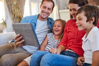 <strong>家庭娱乐</strong>触摸微笑父母坐着年轻的儿子女儿生活房间沙发首页数字平板电脑