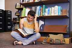 他研究硬即将到来的决赛年轻的大学学生坐着地板上图书馆阅读