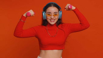 年轻的适合女人听音乐耳机工作泵手臂肌肉提升哑铃