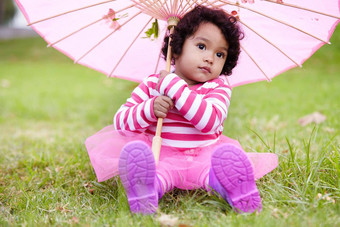 花俏的可爱的女孩坐着草粉红色的伞