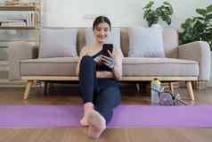 健康的亚洲女人练习放松瑜伽首页支出时间玩电话首页概念