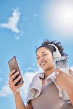 耳机电话女人水瓶在户外流媒体音乐广播音频社会媒体网络低角女移动文本消息培训运行锻炼