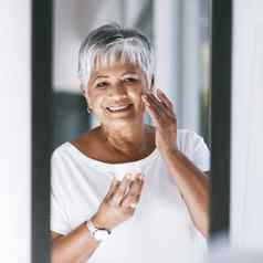 皮肤辐射快乐的成熟的女人应用皮肤奶油脸镜子首页