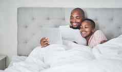 平板电脑卧室黑色的夫妇流媒体在线订阅服务床上放松社会媒体娱乐视频男人。女人放松早....