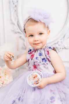 婴儿女孩优雅的衣服一岁女孩蓬松的衣服可爱的弓提出了背景明亮的房间沙拉酱表格花