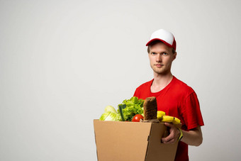 一边视图交付男人。红色的统一的交付食物食品杂货蔬菜饮料纸盒子客户端首页在线杂货店购物服务概念