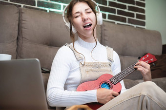 年轻的女人学生学习人声玩尤克里里琴首页坐着地板上生活房间前面移动PC