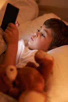 光阅读床上年轻的男孩玩平板电脑说谎床上