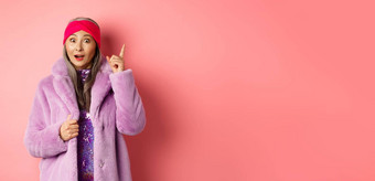 时尚购物概念微笑上了年纪的女人的想法时尚的夫人紫色的假的皮毛外套提高指数手指建议计划站兴奋粉红色的背景