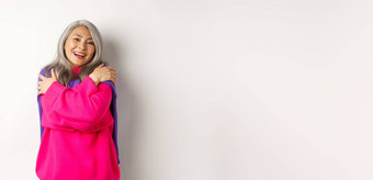 情人节一天假期概念可爱的亚洲高级女人粉红色的毛衣拥抱眼睛关闭微笑站白色背景