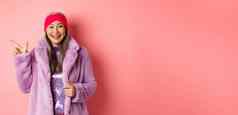 时尚购物概念快乐亚洲高级女人检查时尚的促销活动指出手指左标志微笑穿冬天假的皮毛外套头巾