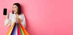 有吸引力的亚洲女人显示智能手机应用程序购物袋购买在线应用程序站粉红色的背景
